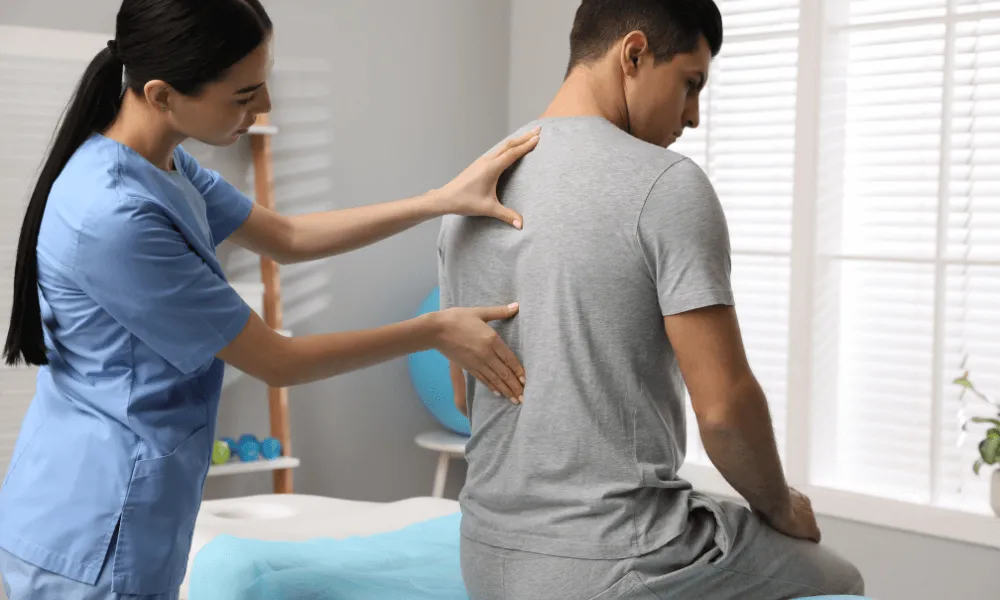 A healthcare professional assists a patient by examining their back in a treatment setting.